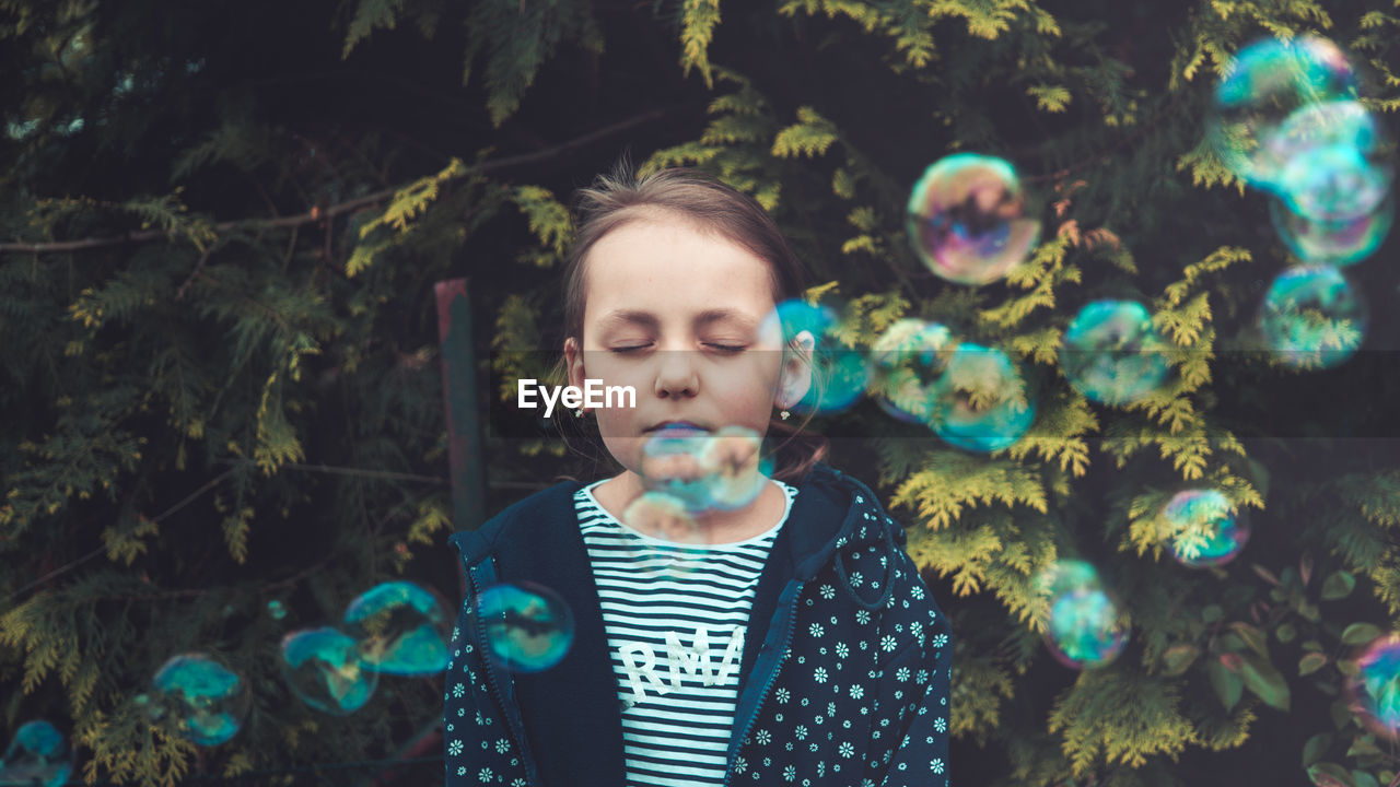 Girl with closed eyes standing amidst bubbles against plants