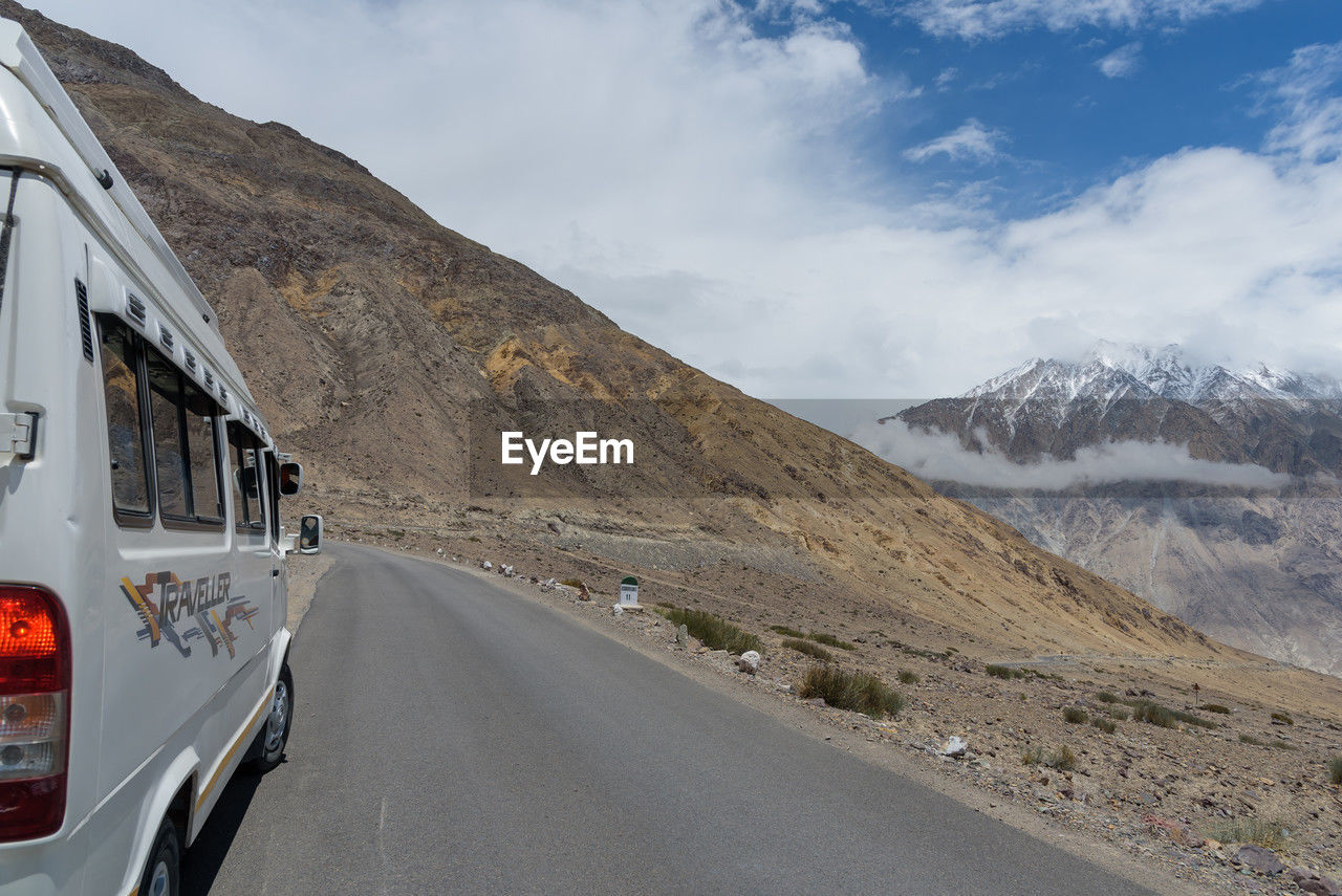 transportation, mountain, mode of transportation, road, mountain range, motor vehicle, road trip, mountain pass, landscape, sky, environment, scenics - nature, nature, travel, cloud, car, snow, beauty in nature, vehicle, land, land vehicle, no people, cold temperature, highway, journey, travel destinations, snowcapped mountain, non-urban scene, day, winter, outdoors, on the move, motion, transport, the way forward