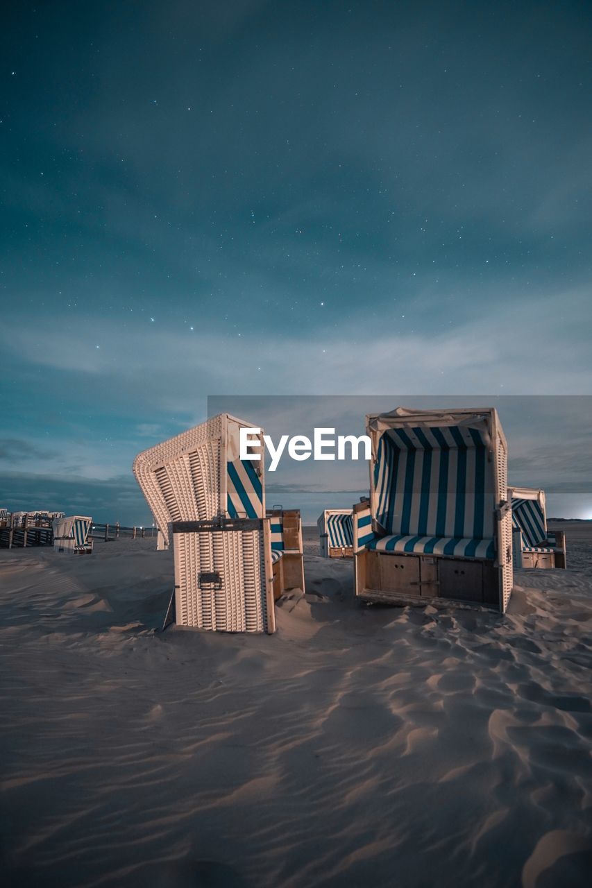 Hooded chairs at beach against sky at dusk