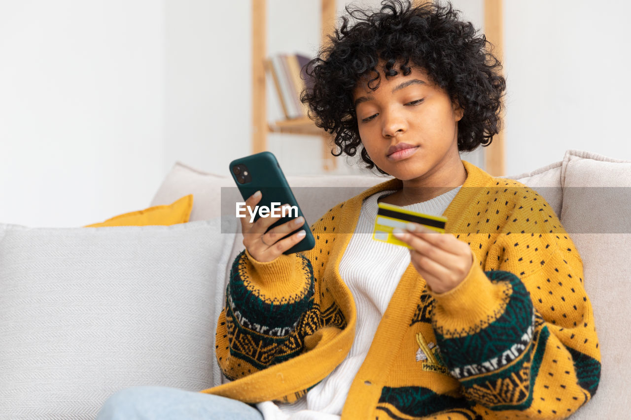 young woman using mobile phone while sitting on sofa at home