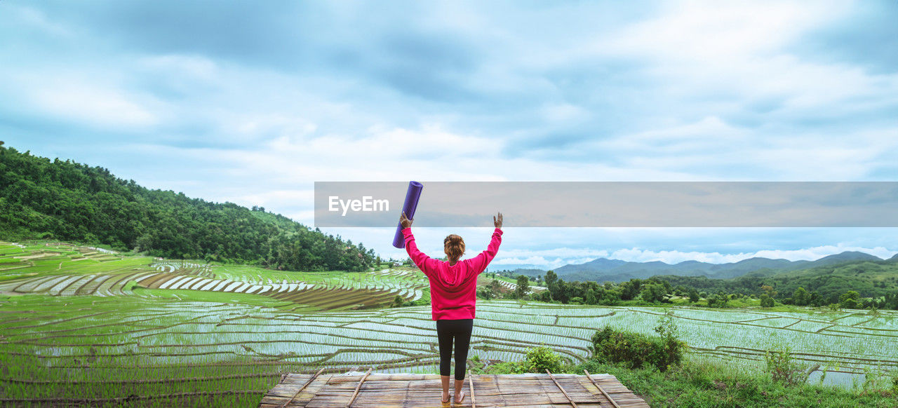 rear view of woman with arms outstretched standing on landscape against sky