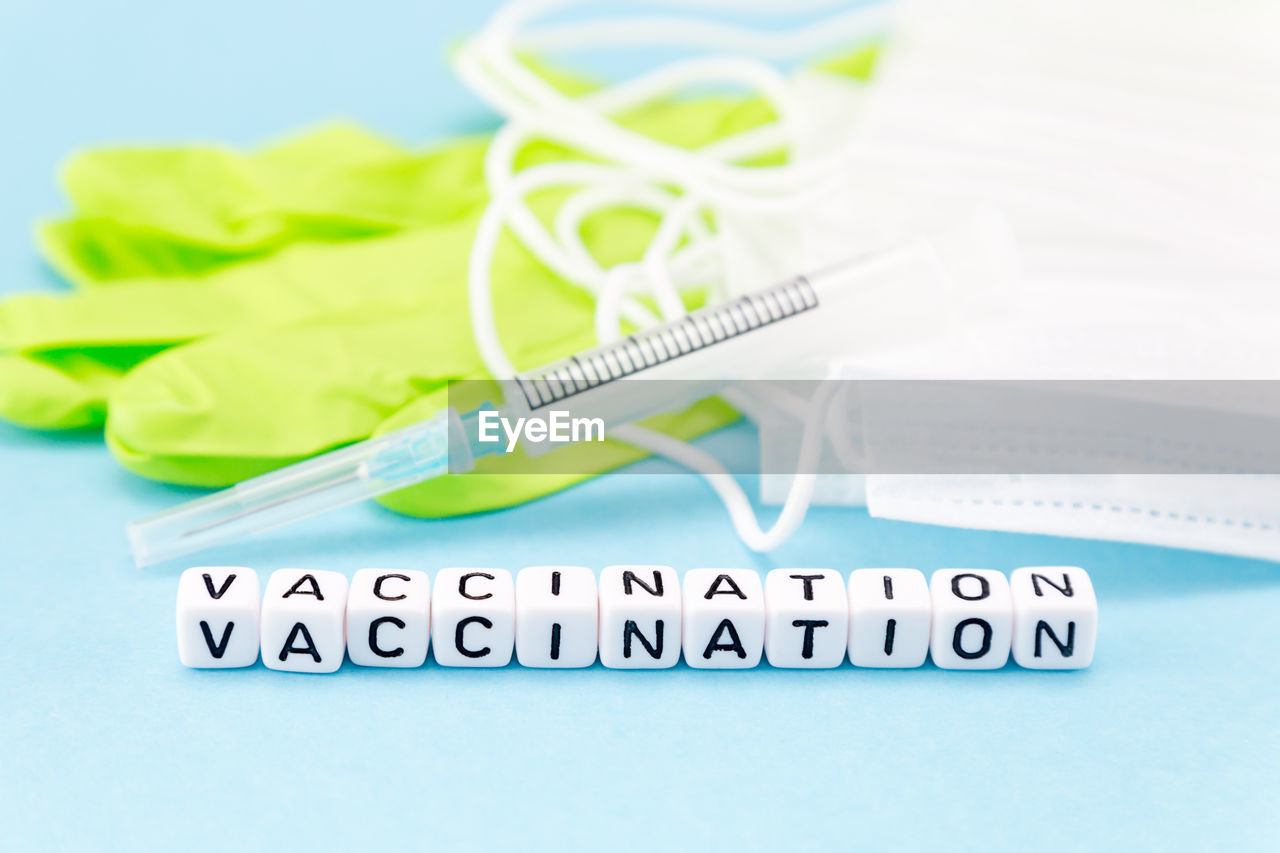 Medical masks, gloves, syringe and the word vaccination composed with cubes on a blue background