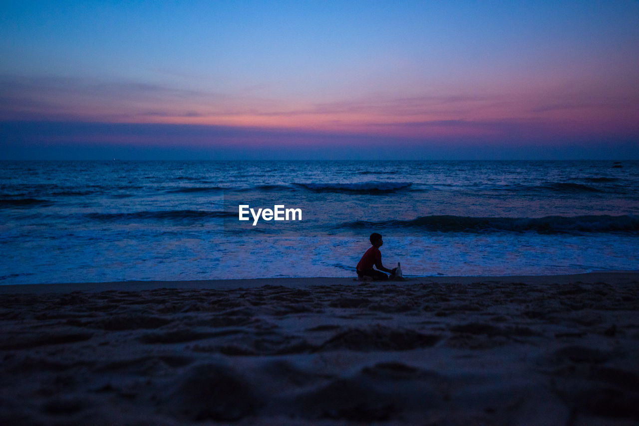 Silhouette boy playing at beach against sky during sunset