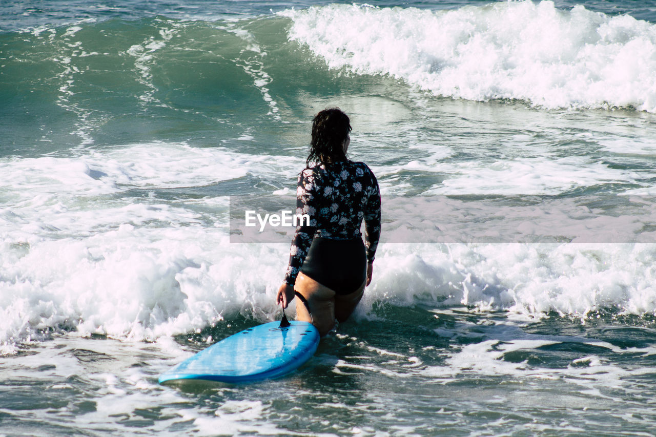 REAR VIEW OF MAN IN SEA AGAINST WAVES