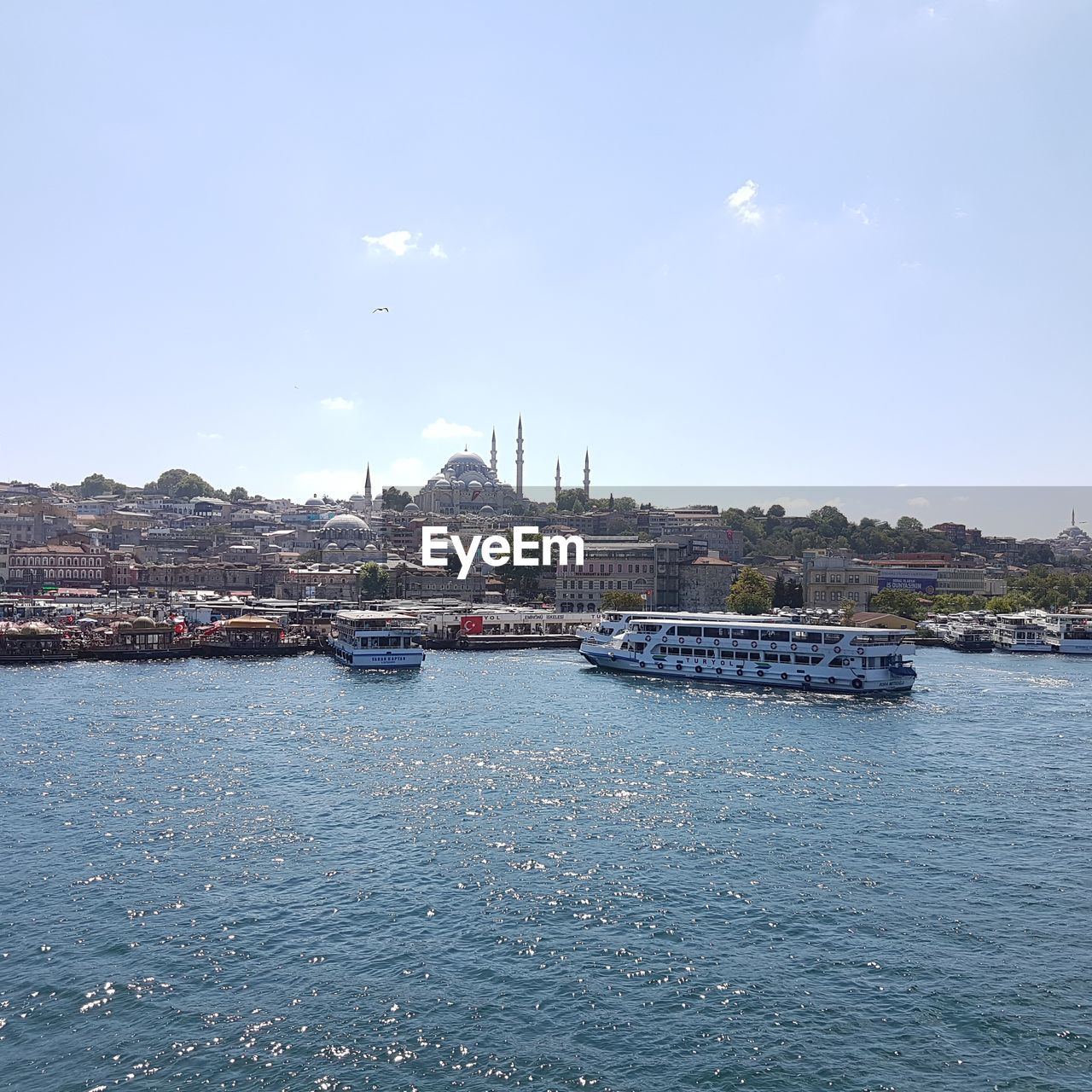 SAILBOATS MOORED IN HARBOR AGAINST CITYSCAPE