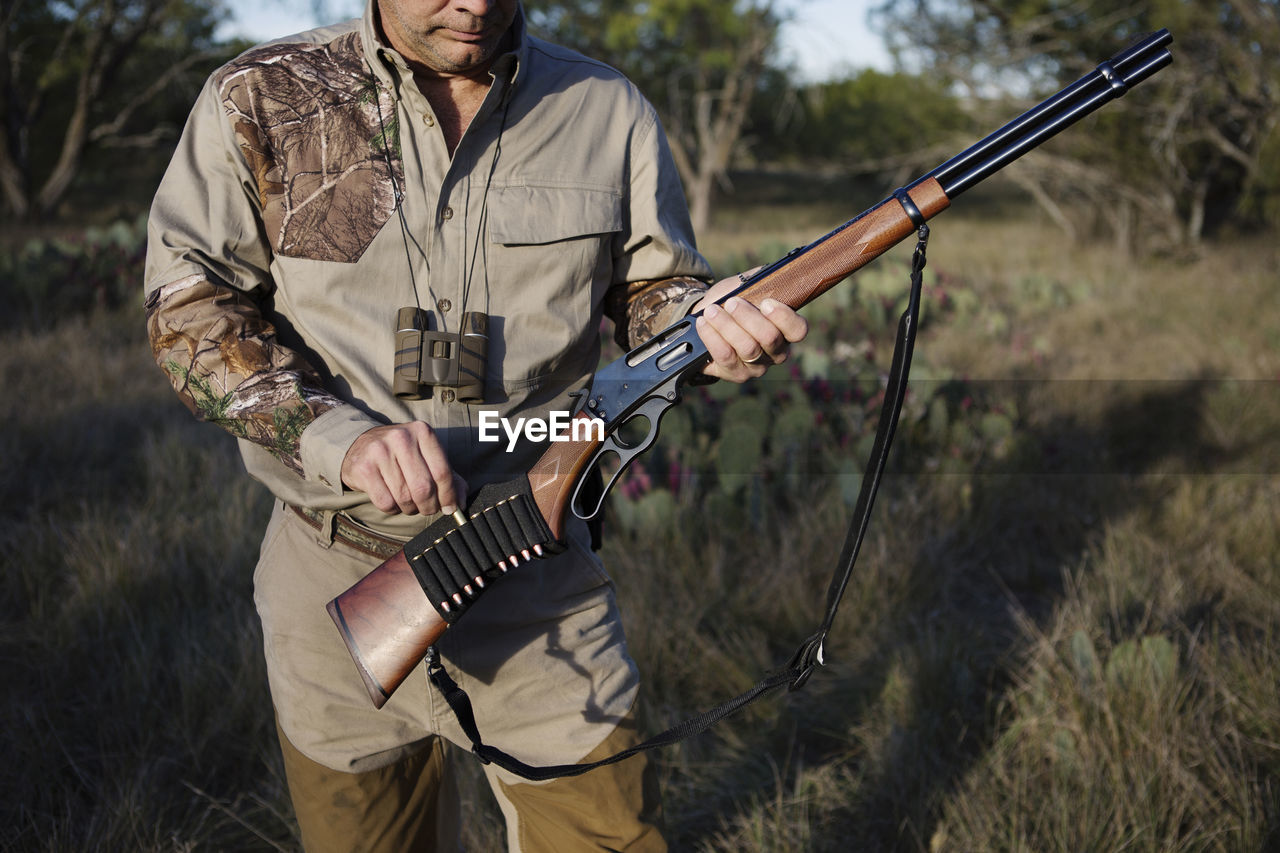 Midsection of man loading bullet in rifle on grassy field