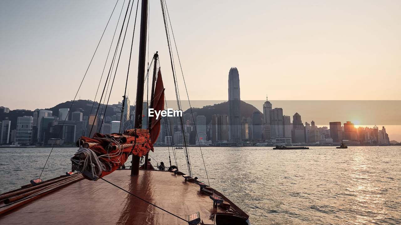 Traditional junk boat crossing victoria harbour against hong kong skyline at sunset.