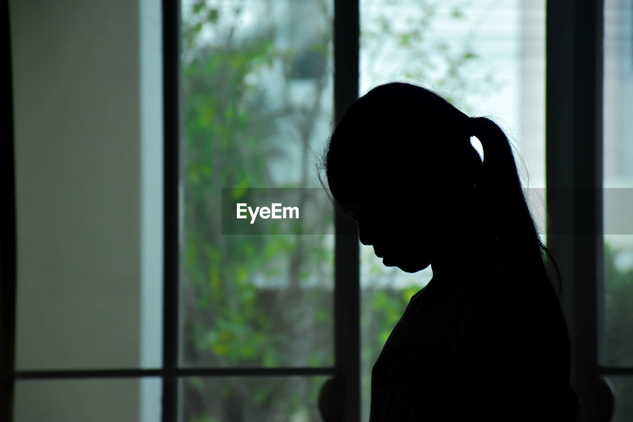 Close-up of silhouette woman against window at home