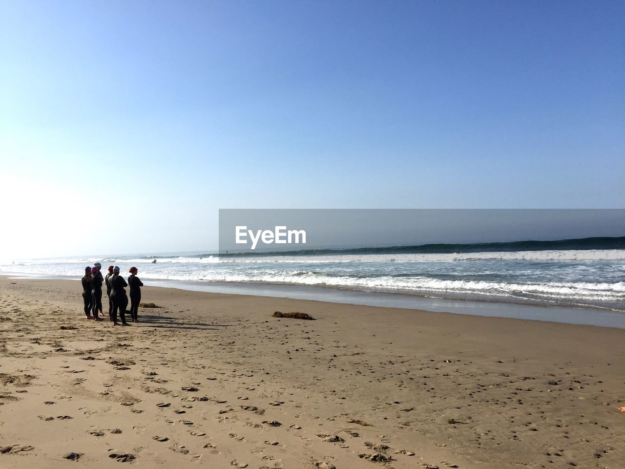 People wearing wetsuit while standing on shore at beach against clear sky