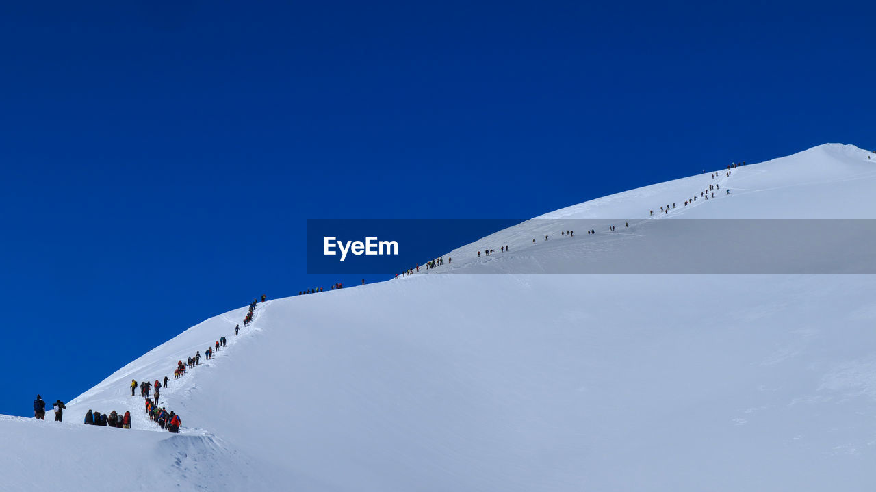 Low angle view of people on snowcapped mountain against clear blue sky