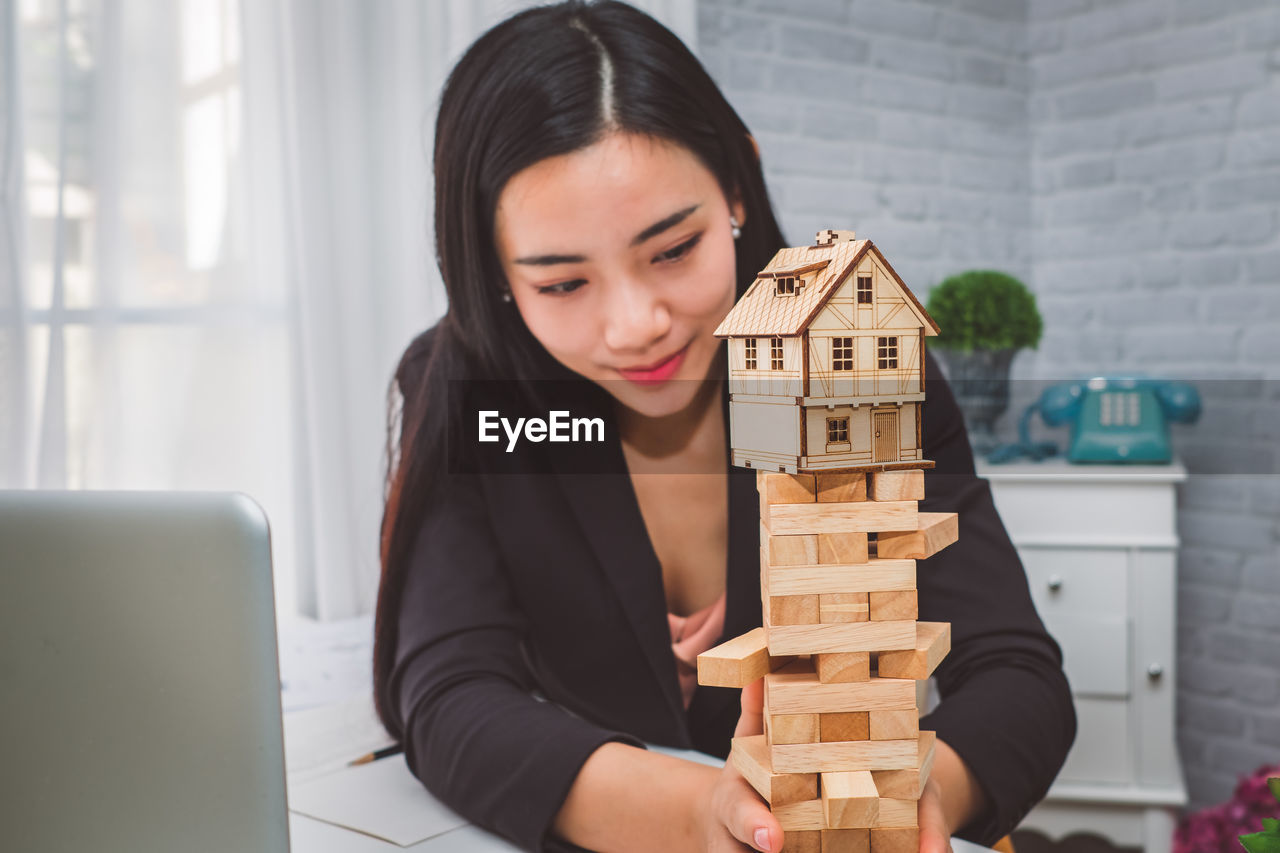 Businesswoman with model home on block removal game at desk