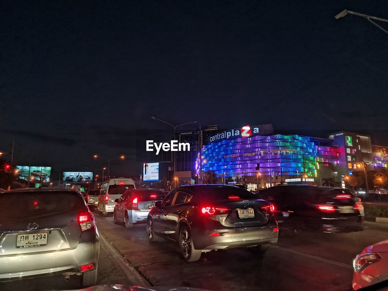 CARS ON ROAD BY ILLUMINATED BUILDINGS AGAINST SKY AT NIGHT