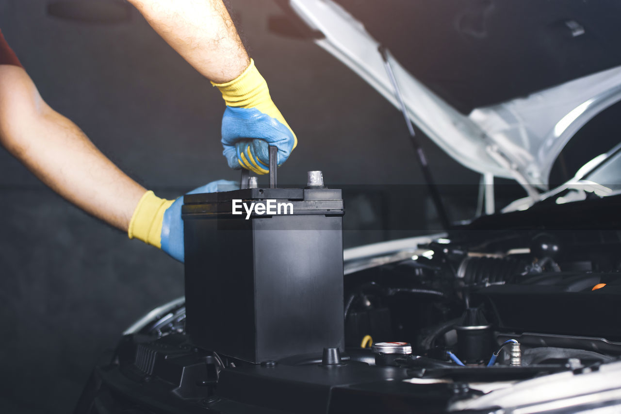 The auto mechanic hand is pulling up an car old battery for new replacement