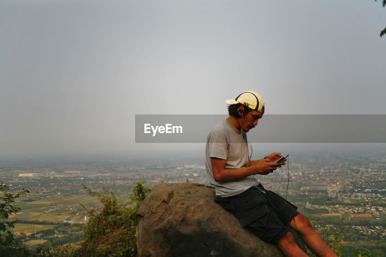 Man sitting on rock in mountain hill against sky