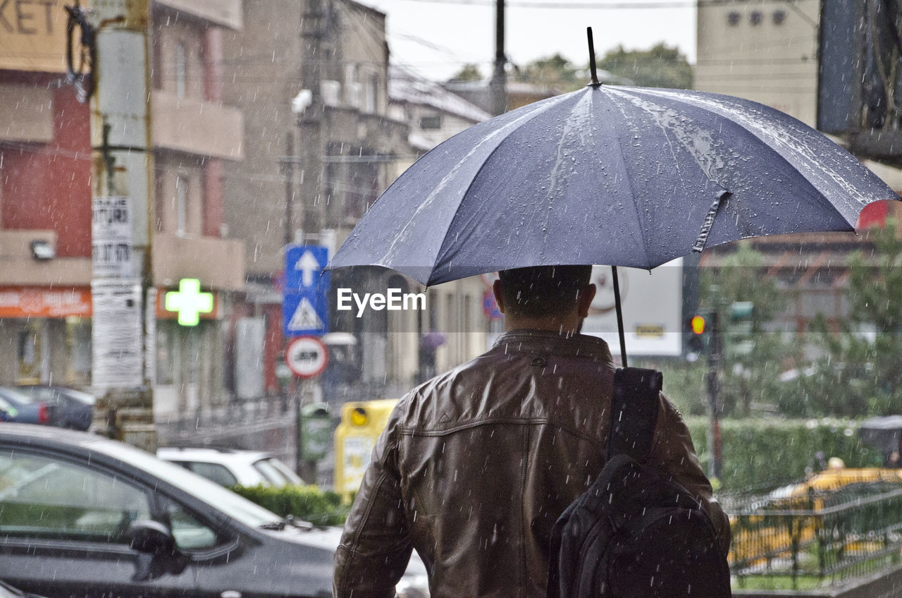 REAR VIEW OF WOMAN HOLDING UMBRELLA WITH RAIN DROPS