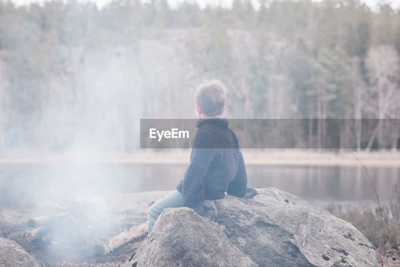 Young boy sitting on a rock by a campfire and lake in sweden