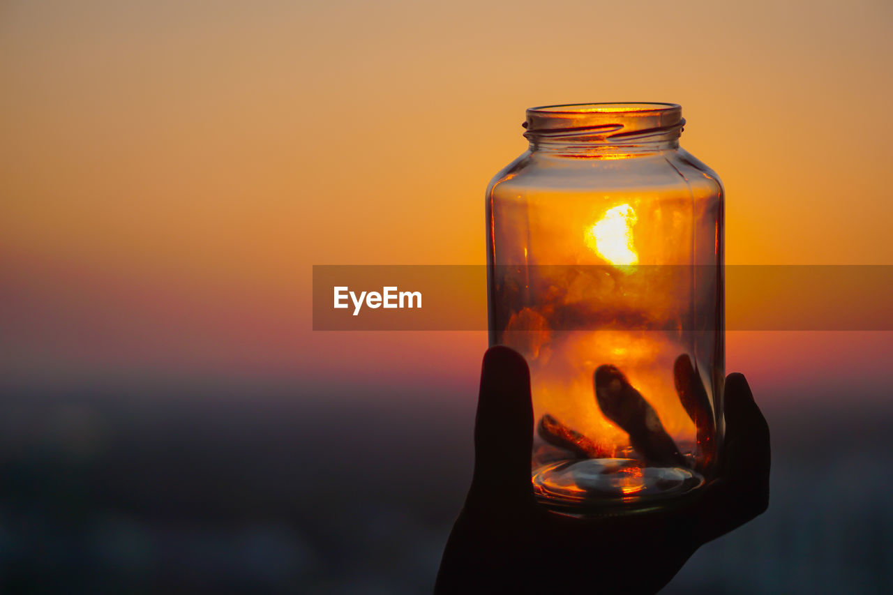 CLOSE-UP OF HAND HOLDING GLASS DURING SUNSET