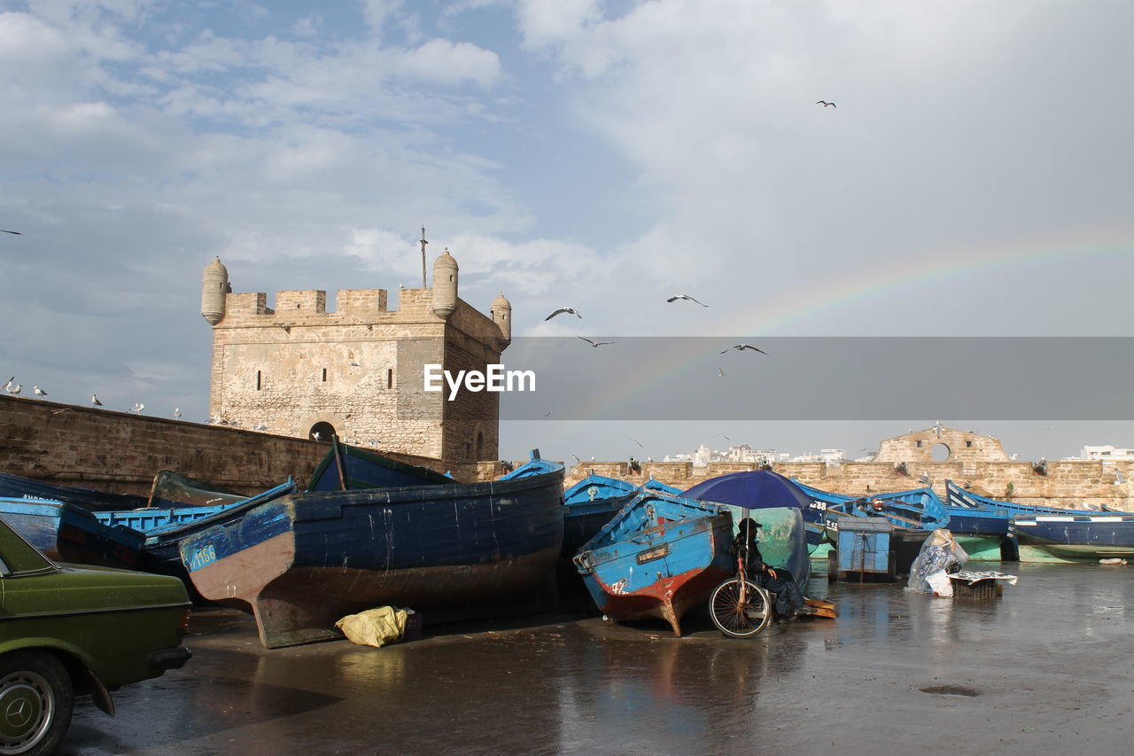 Boats moored on shore by fort during low tide against sky