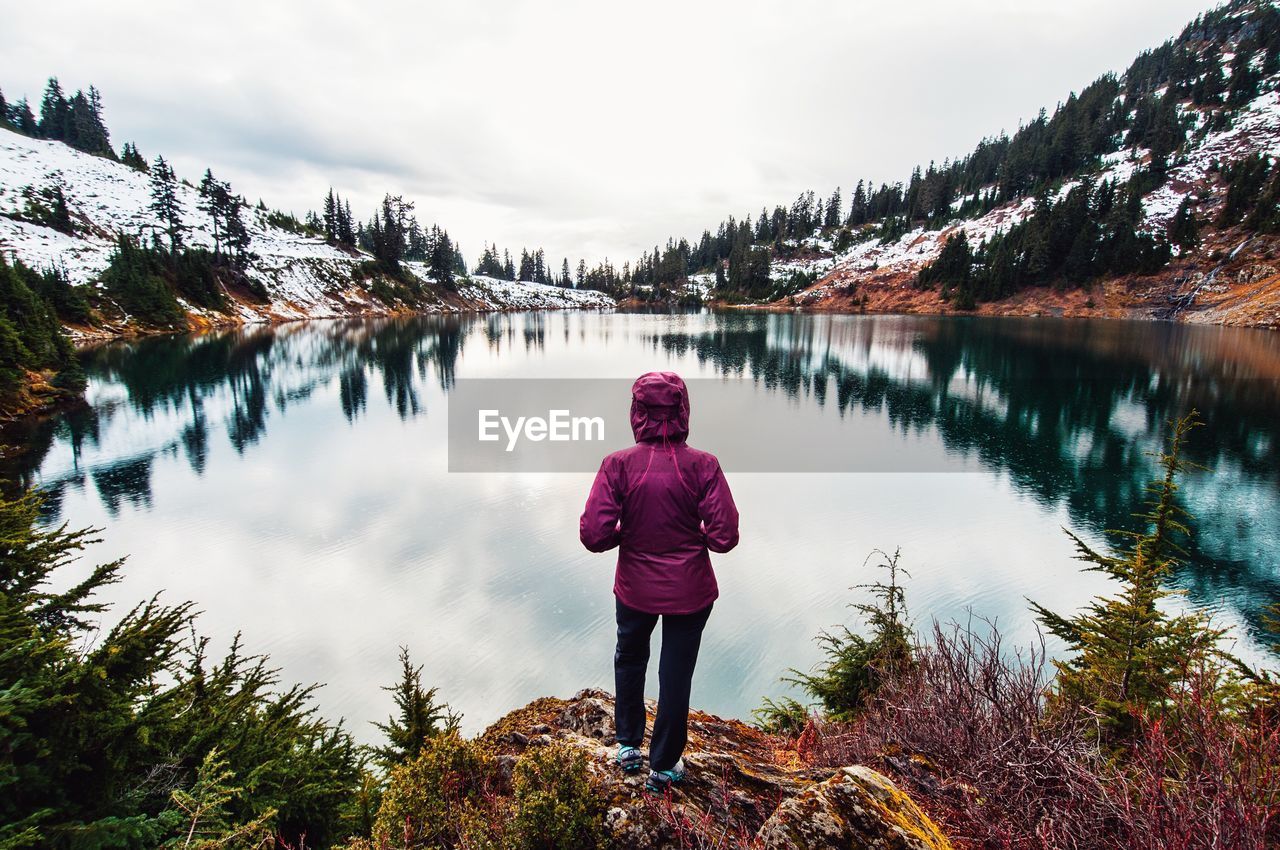 Rear view of woman standing by lake against sky