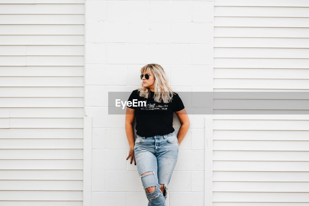 Young woman looking away while standing against white wall