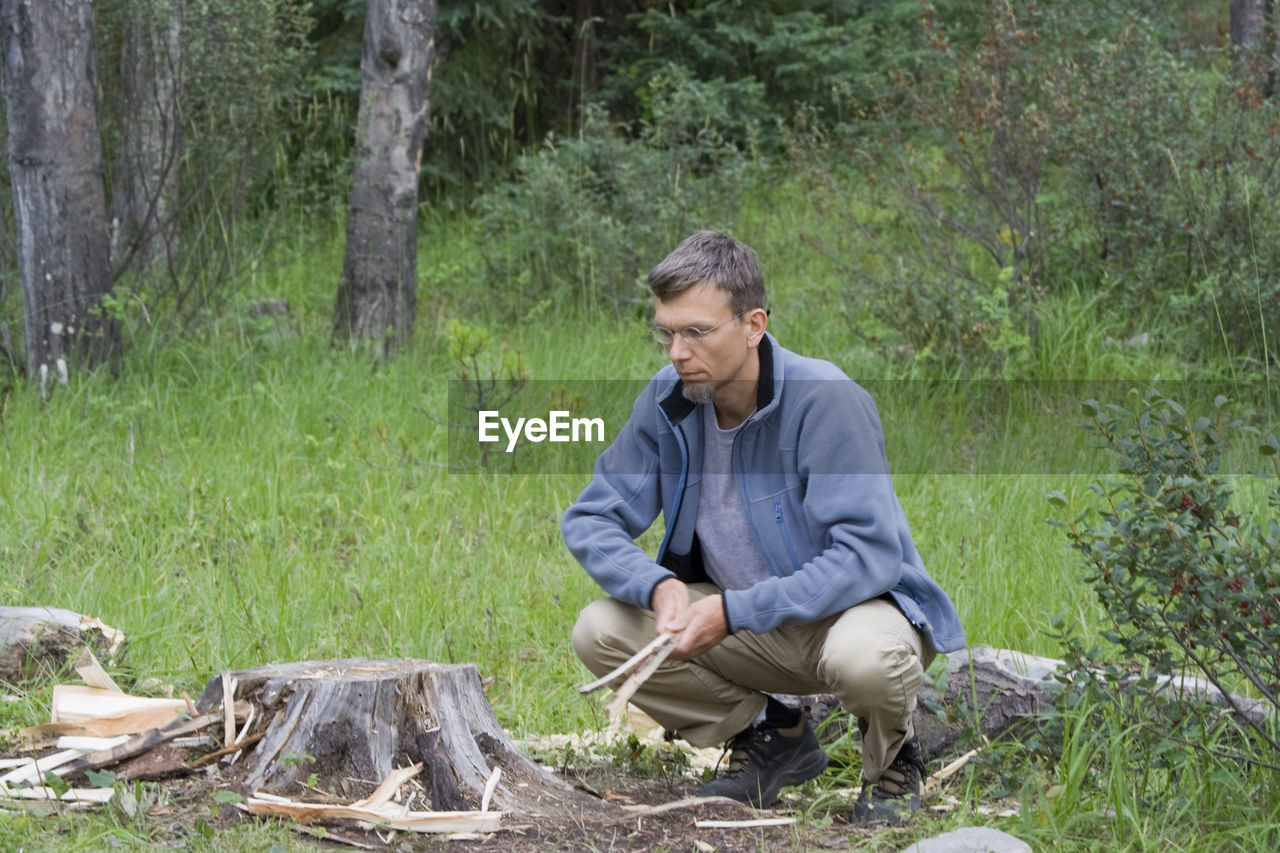 Mature man crouching by tree stump on field at forest