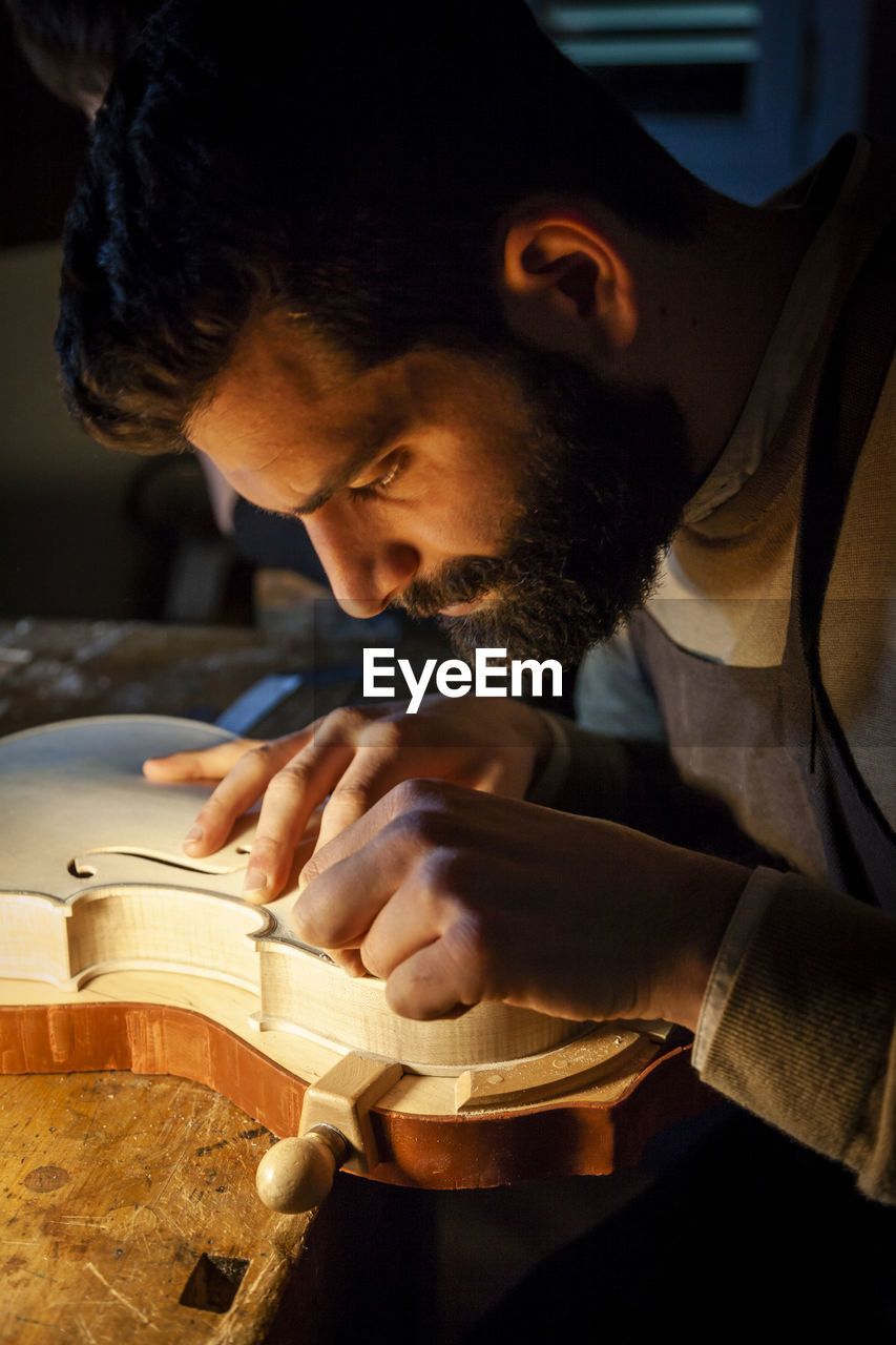 Male craftsman violin maker working on a new violin in the workshop