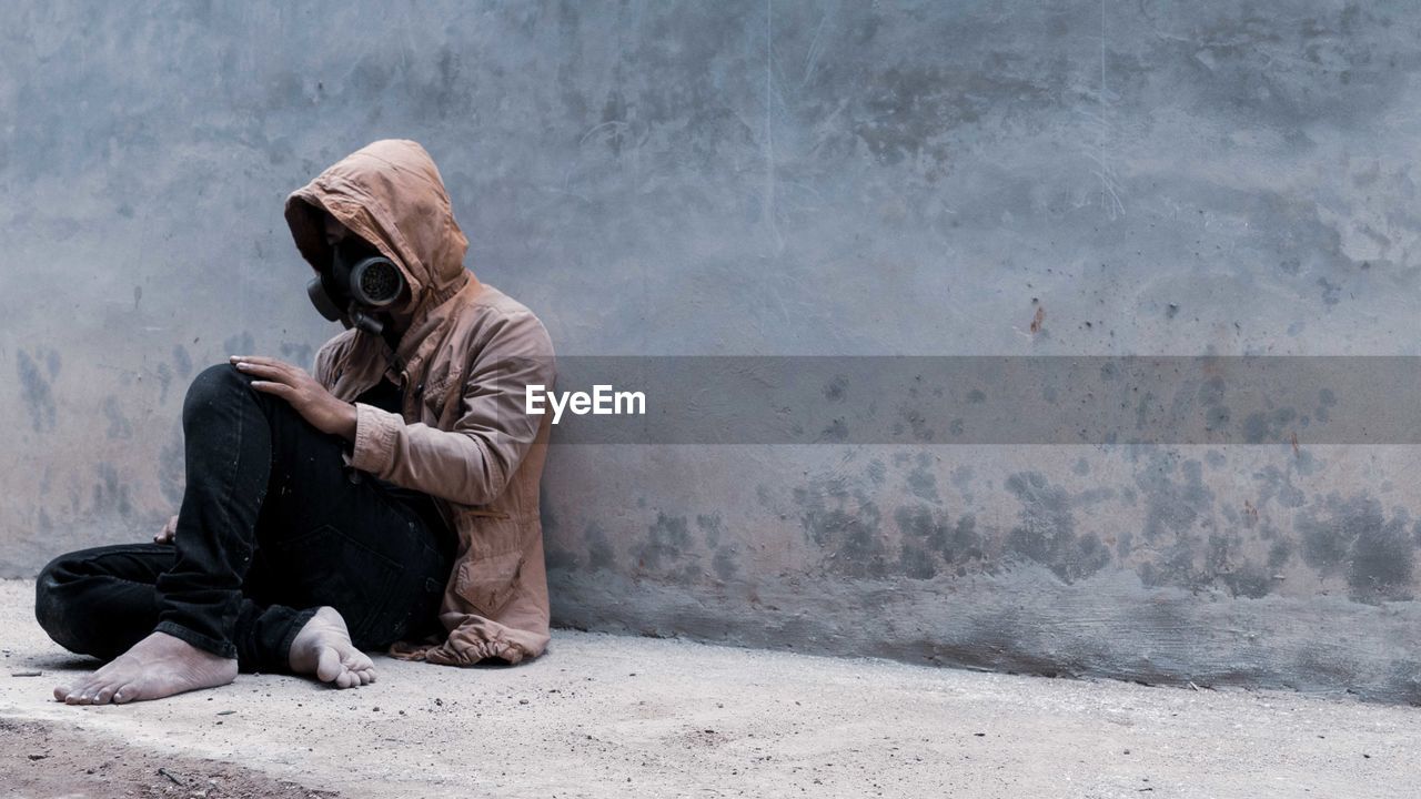 Side view of man sitting against wall