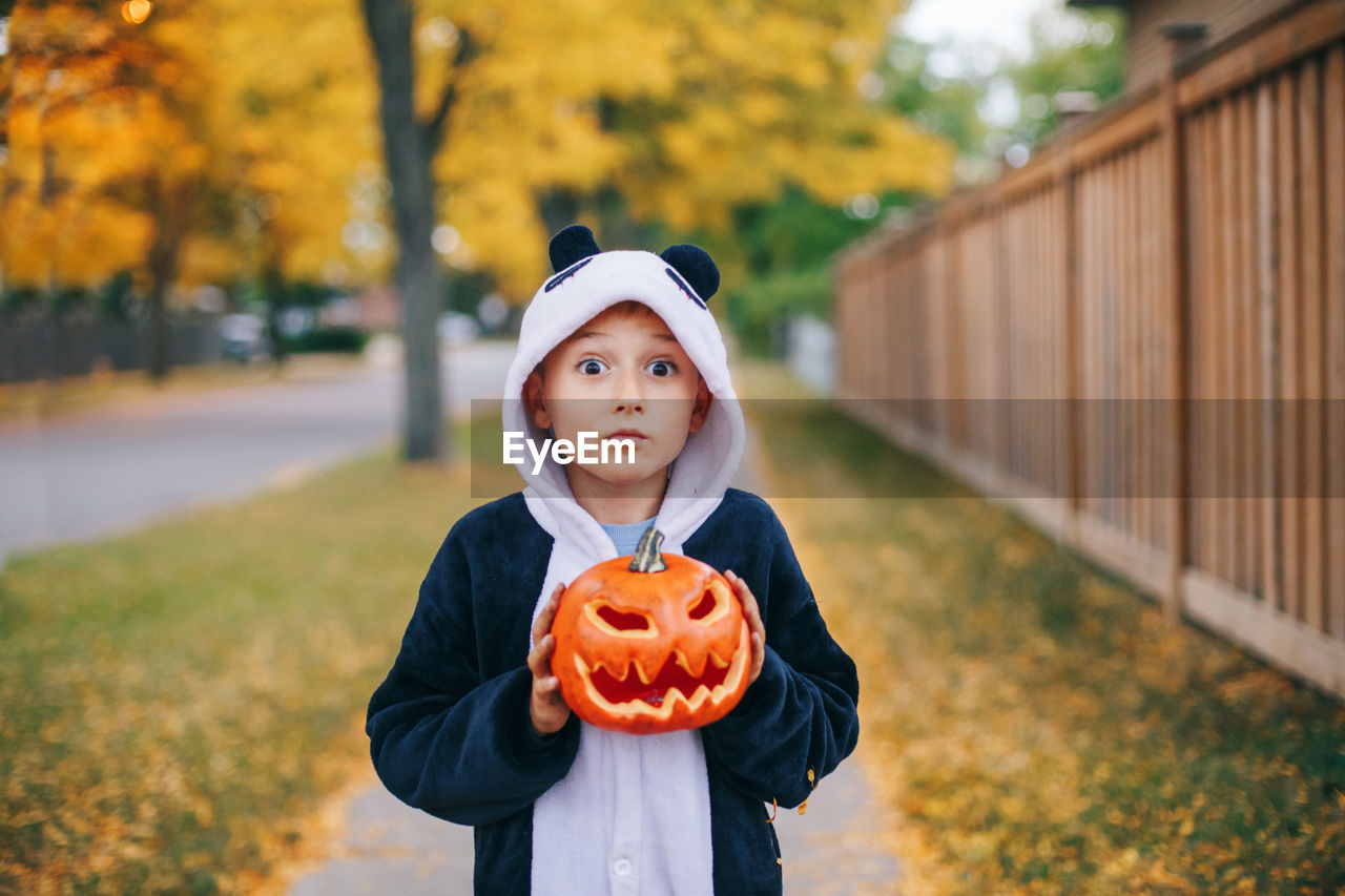 Portrait of cute boy holding pumpkin standing on footpath
