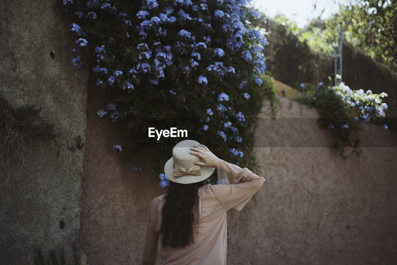 Rear view of teenage girl wearing hat while walking against wall