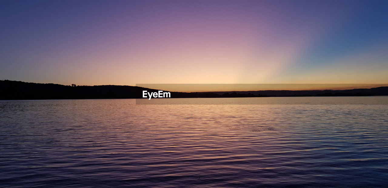 SCENIC VIEW OF LAKE BY SILHOUETTE MOUNTAINS AGAINST SKY DURING SUNSET