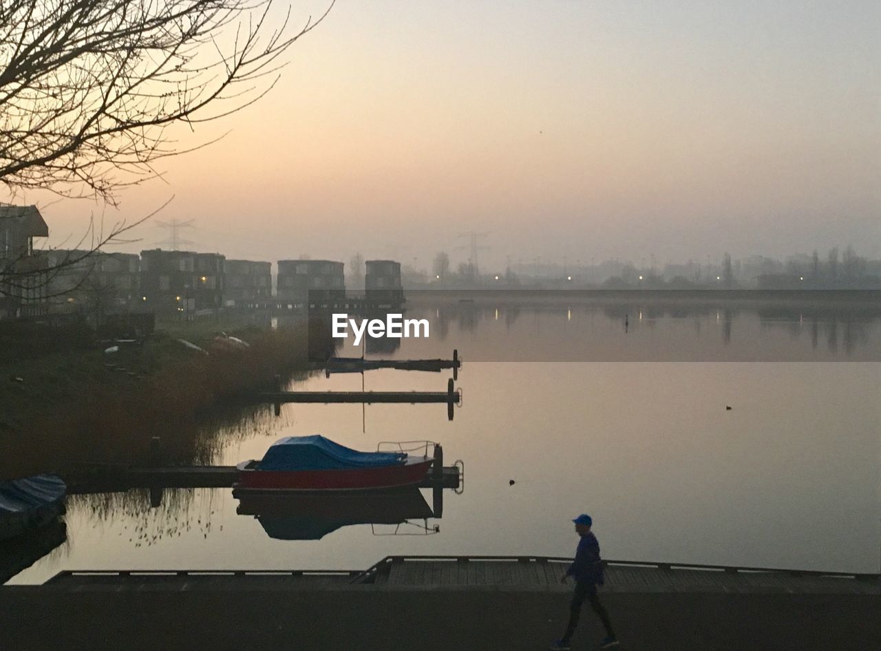 MAN STANDING ON LAKE AGAINST SKY DURING SUNSET