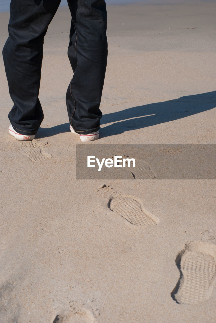 Low section of man standing on sand at beach