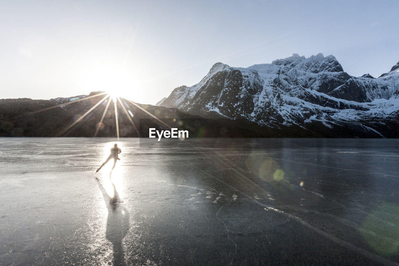 Man ice-skating on frozen lake at sunset