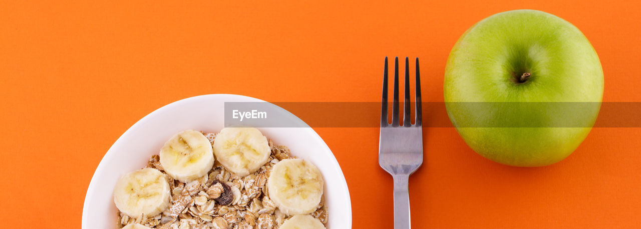 Muesli with banana on orange background with apple