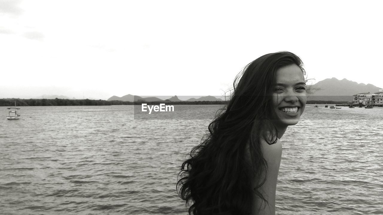 Portrait of smiling young woman standing by sea against clear sky