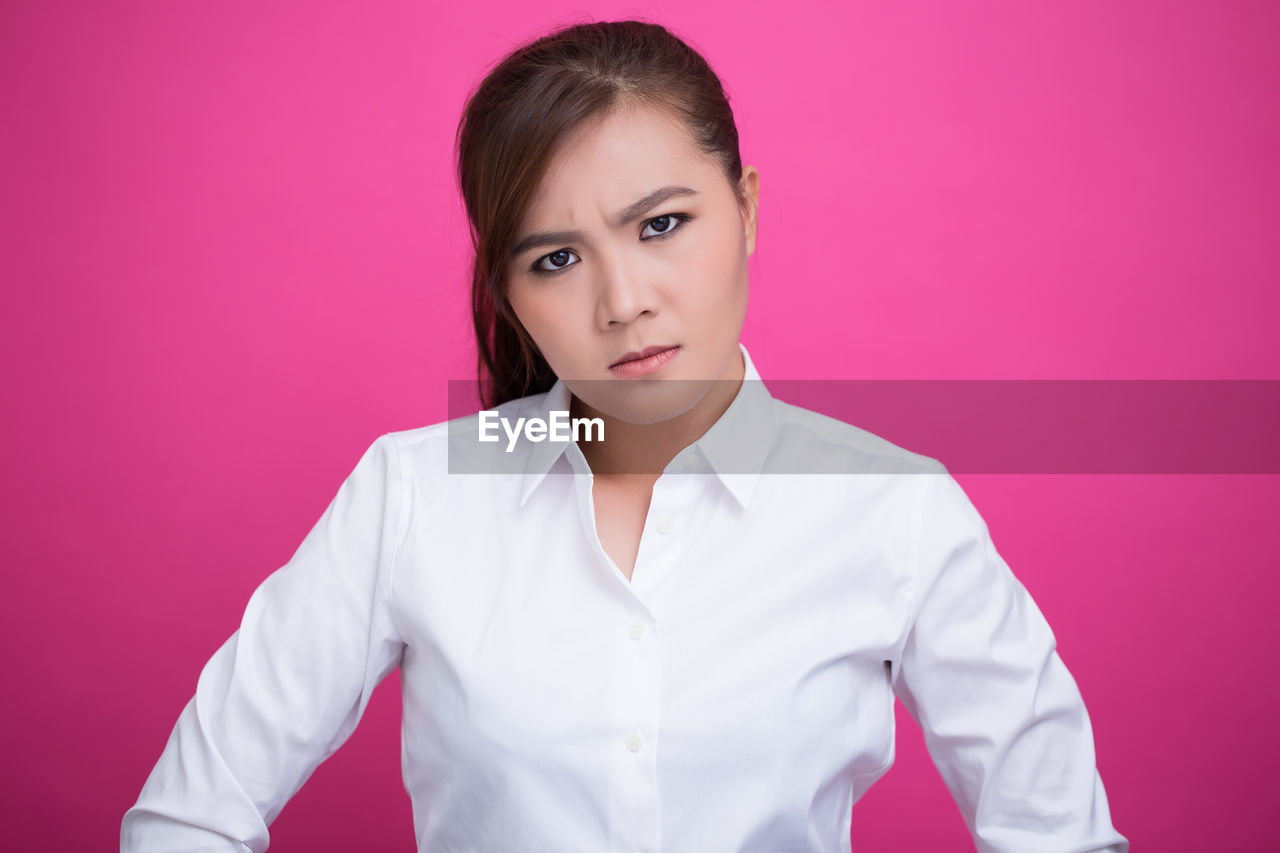 Portrait of angry young woman against pink background