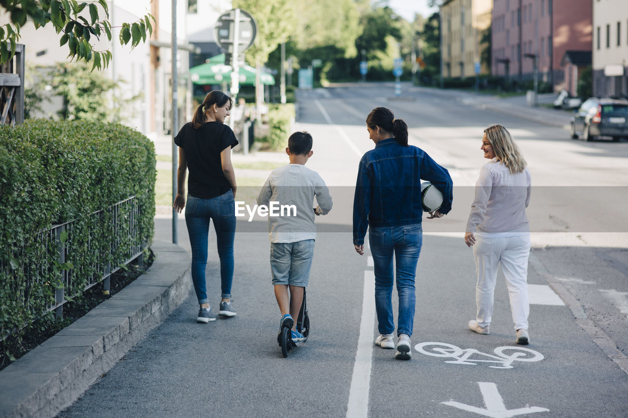 Rear view of family walking on bicycle lane street in city during sunny day