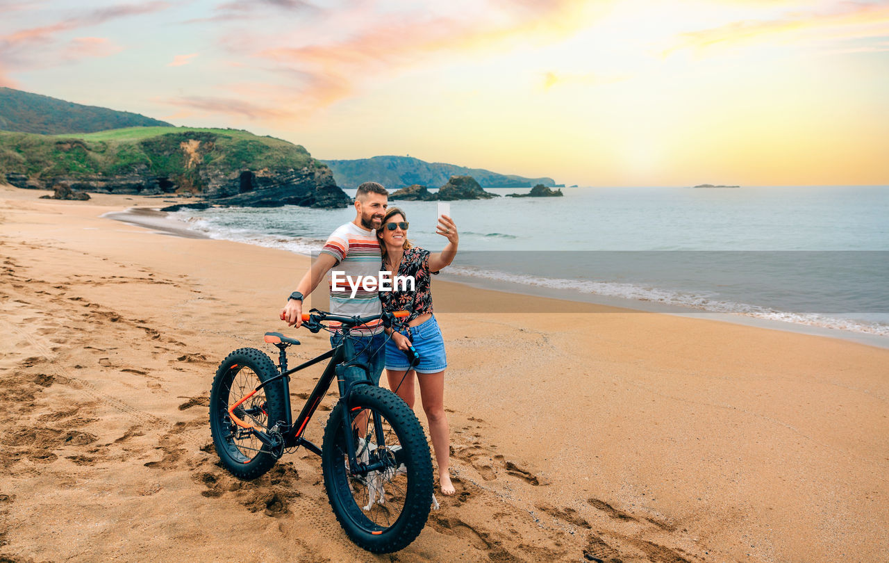 Couple with fat bike taking a selfie with the mobile on the beach