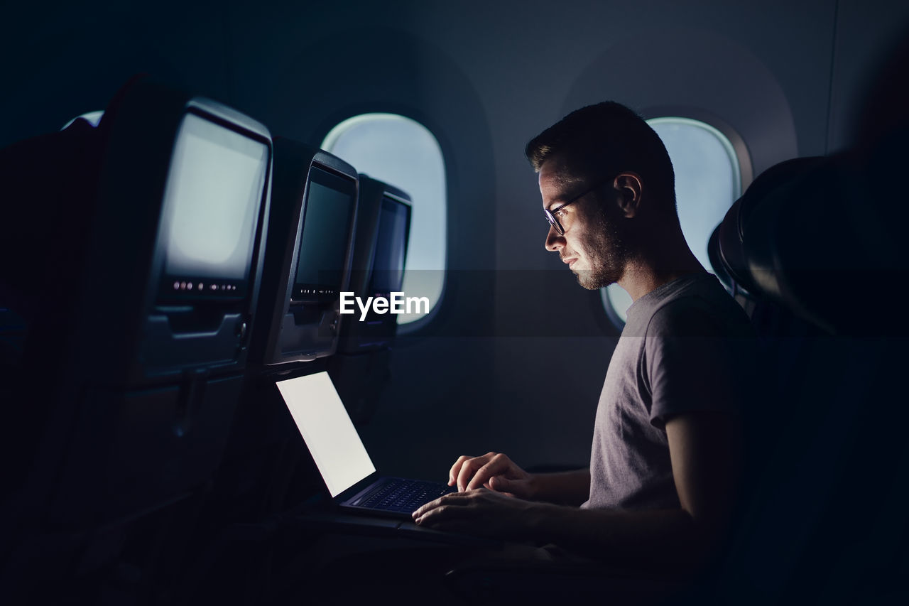 Man traveling by airplane. young passenger using laptop during night flight.