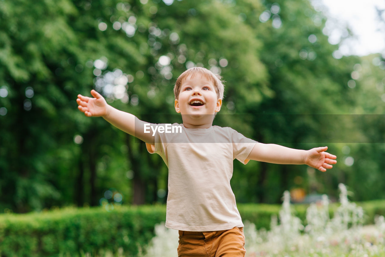 Happy little boy runs with his arms outstretched through the park in summer