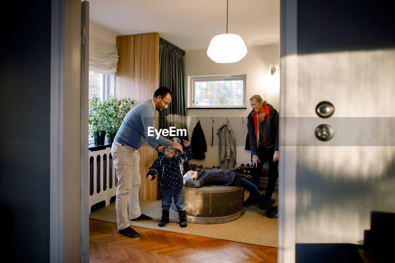 Father helping daughter in getting dressed seen through doorway at home