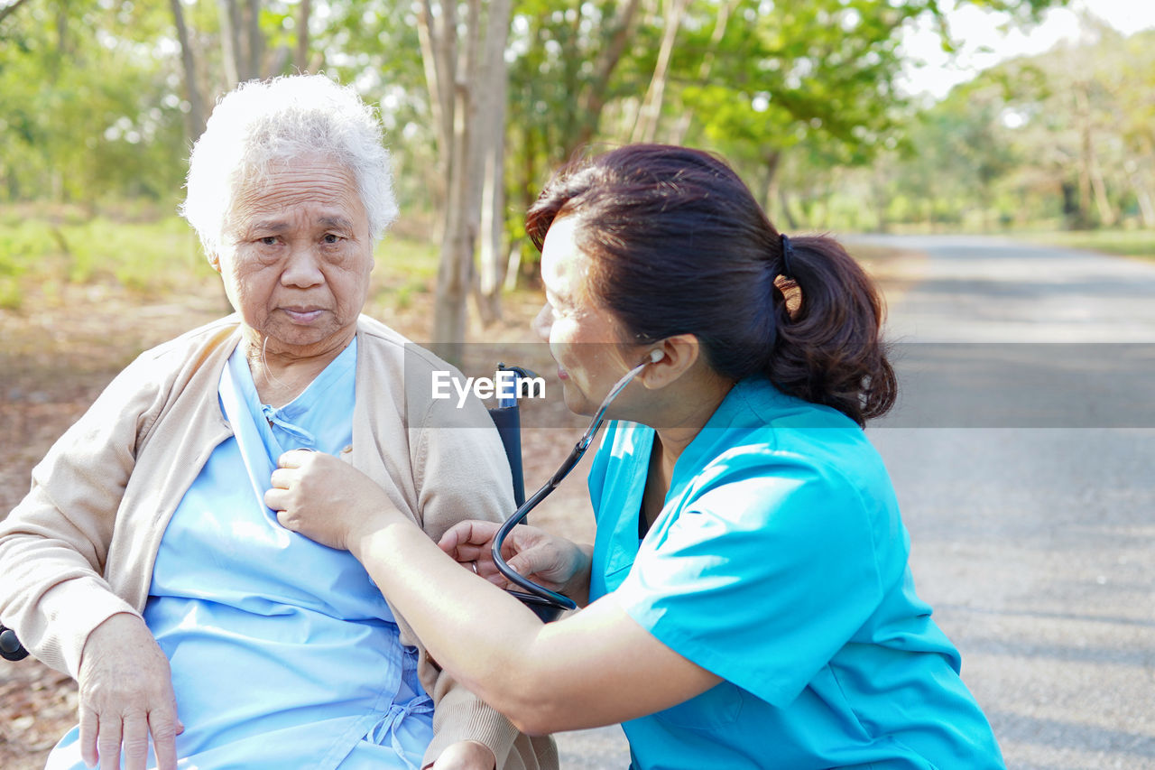 Nurse examining senior female patient sitting on wheelchair at road