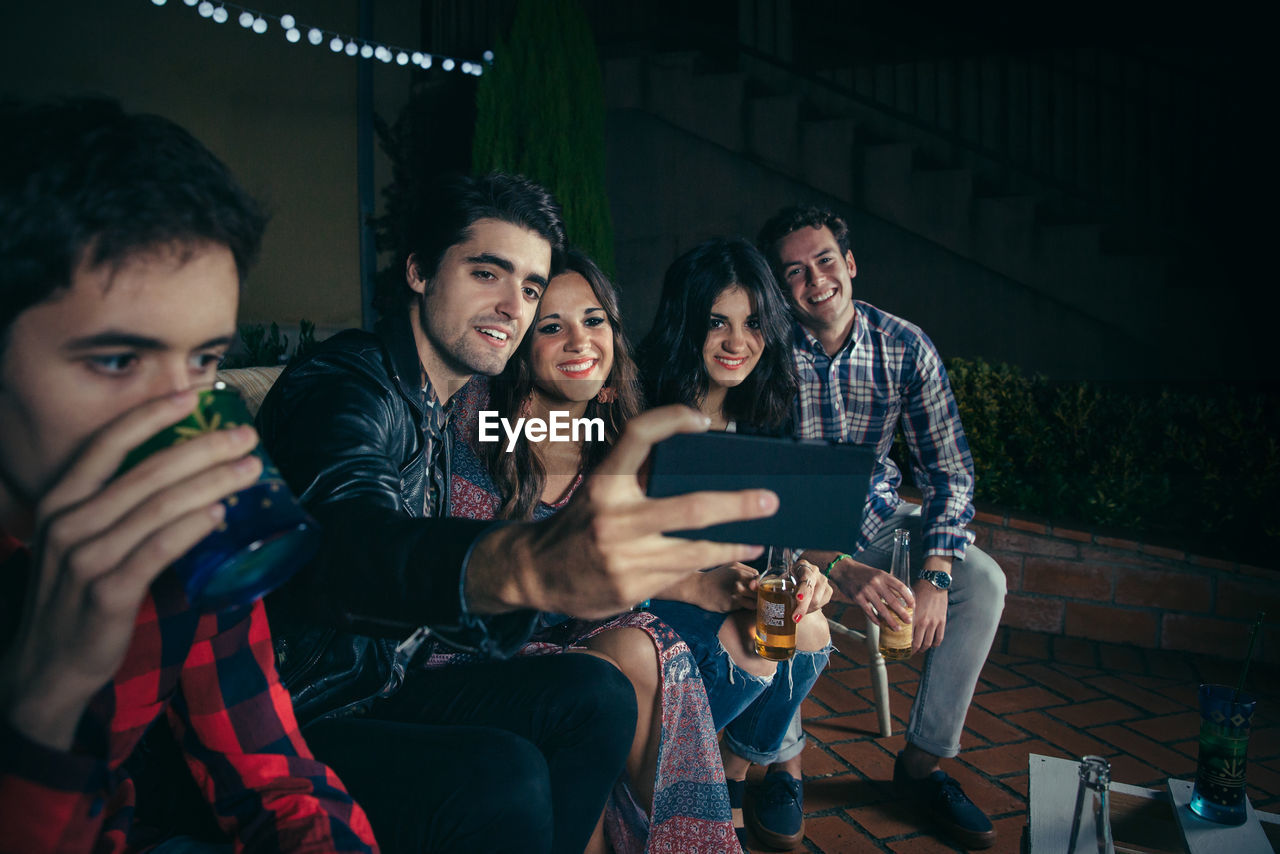 Man having drink with friends taking selfie at patio during night