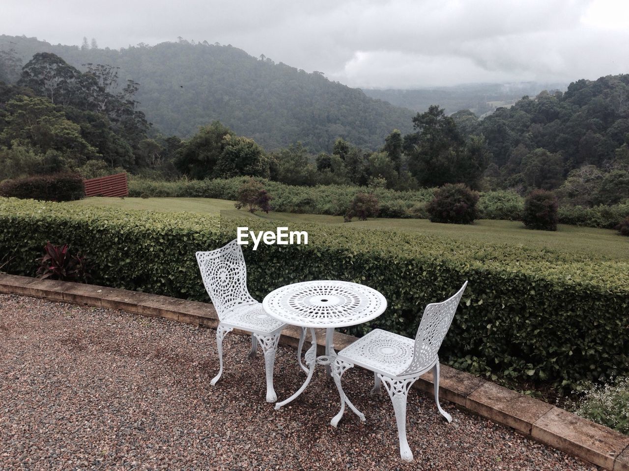 Chairs at table on sidewalk by field