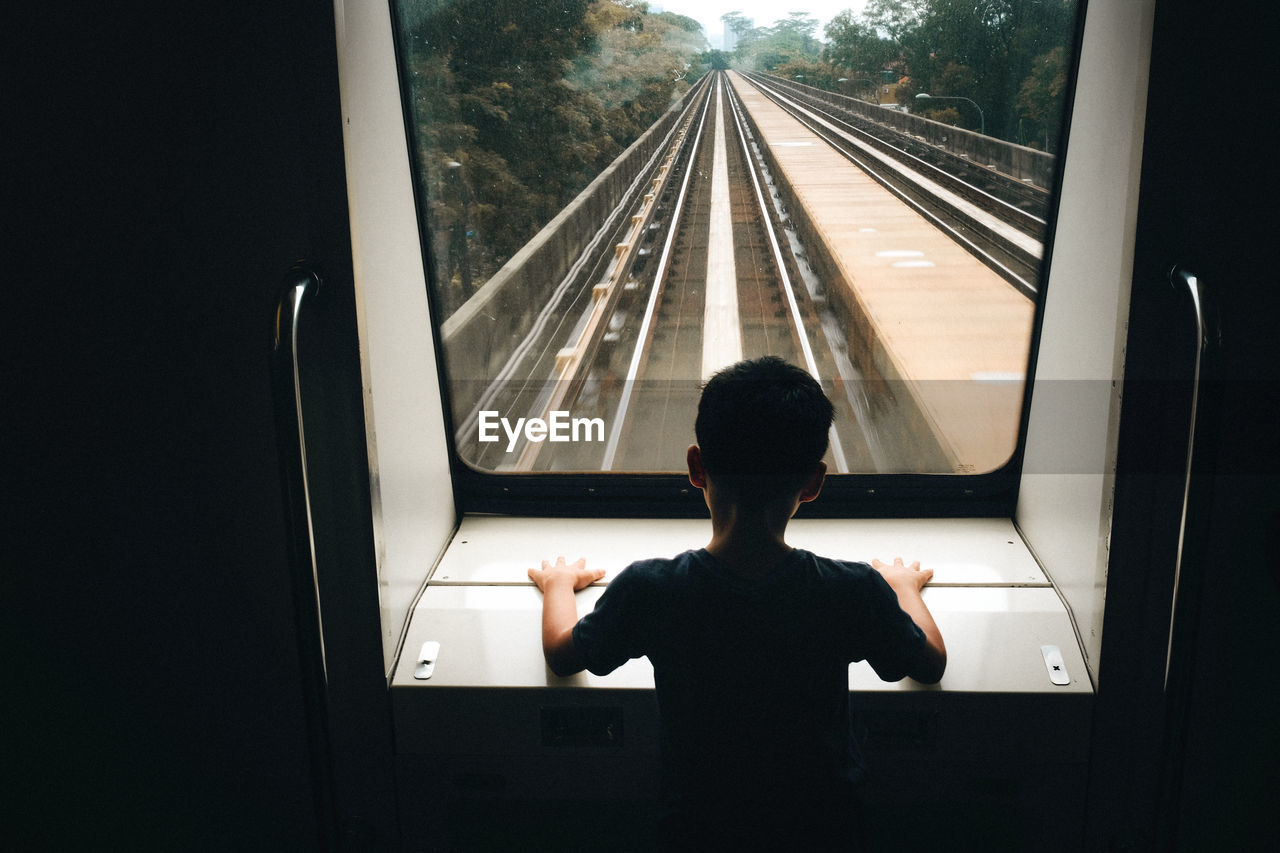 Rear view of boy looking through window in train