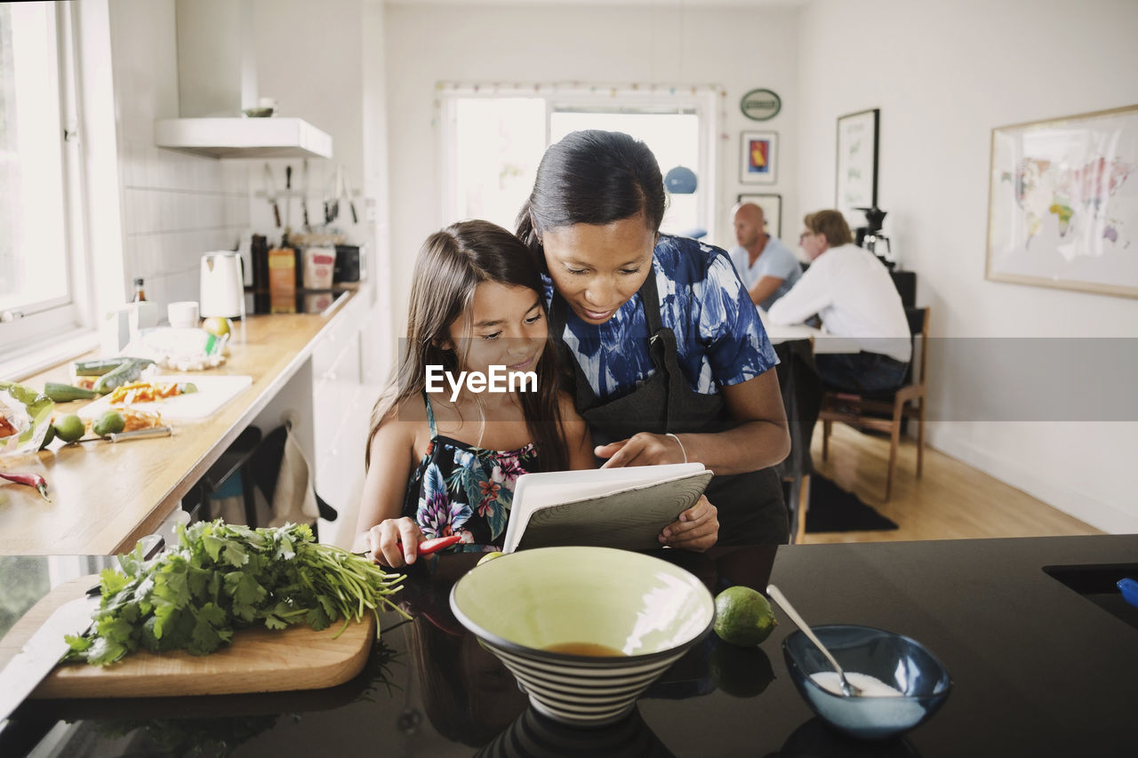 Mother and daughter reading recipe book while cooking in kitchen