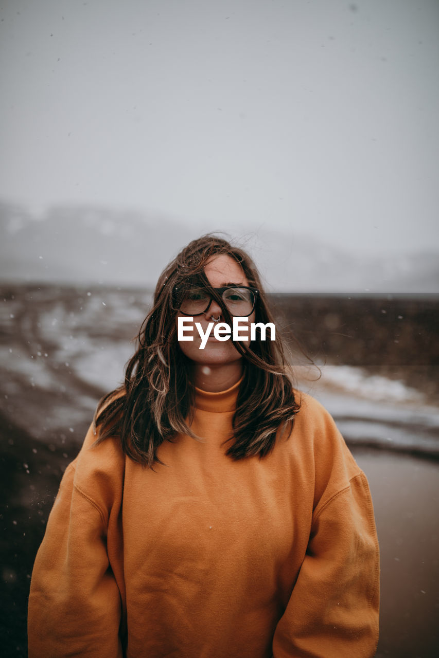 Young happy tourist in eyeglasses with piercing looking at camera between deserted ground in snow