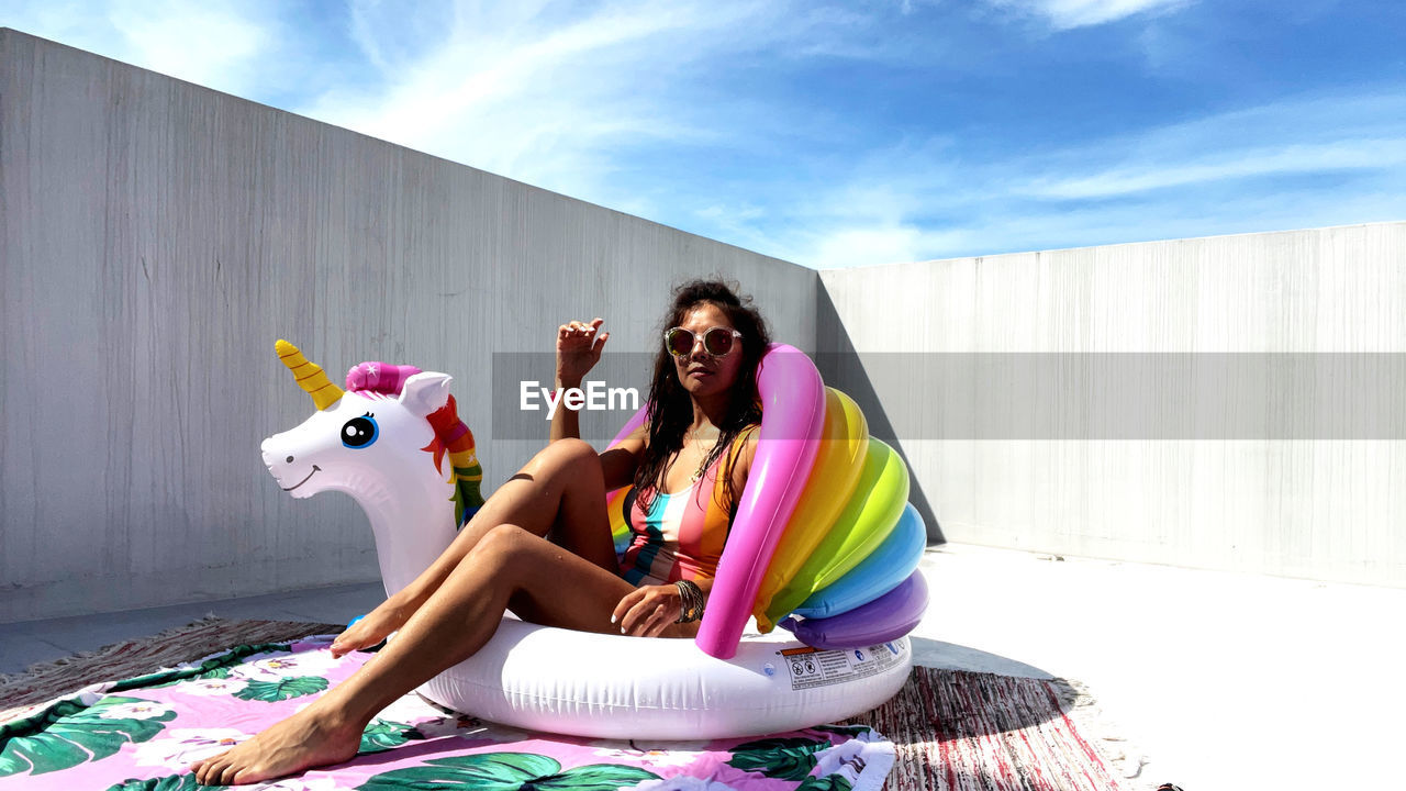 Young woman sitting like poolside against sky with unicorn for fun