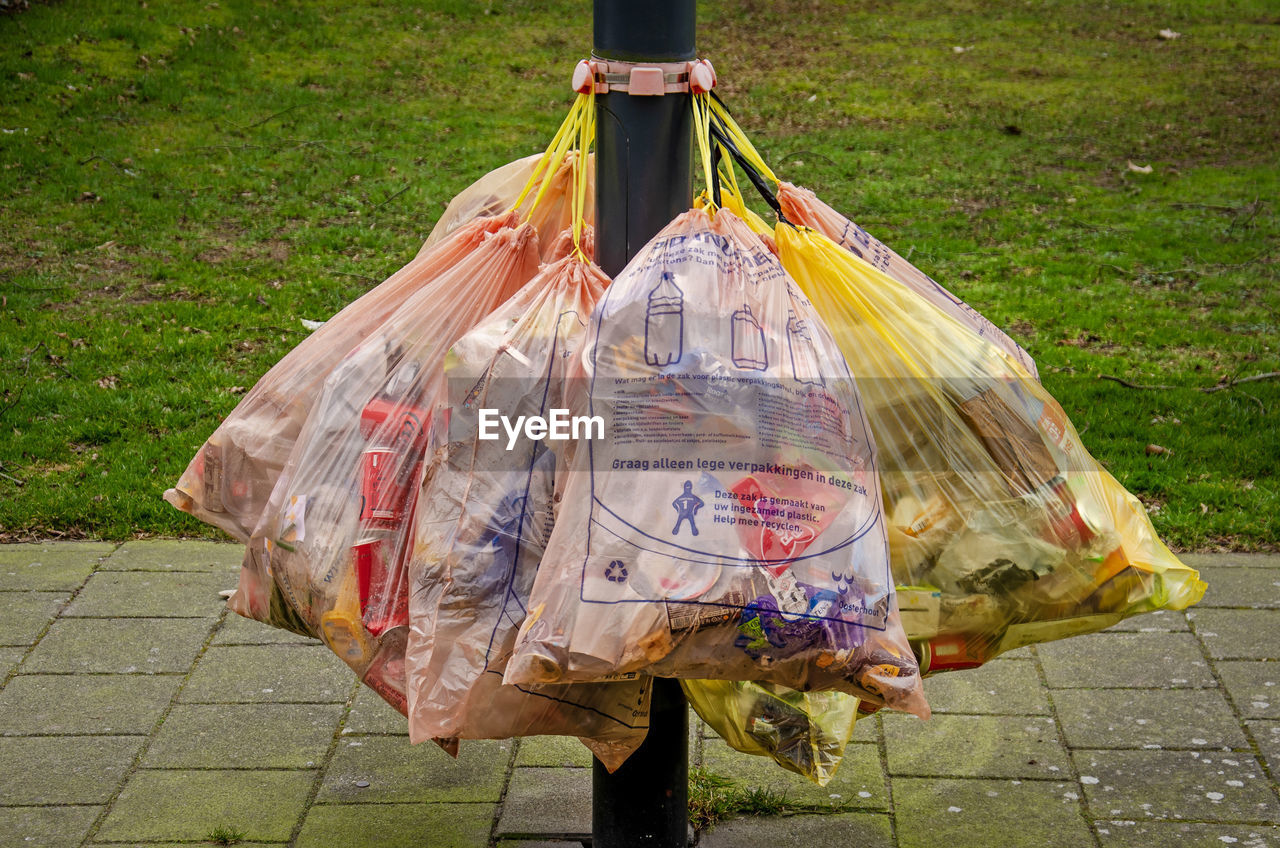 Bags of garbage attached to a lamppost on a sidewalk, waiting to be collected by municipal services