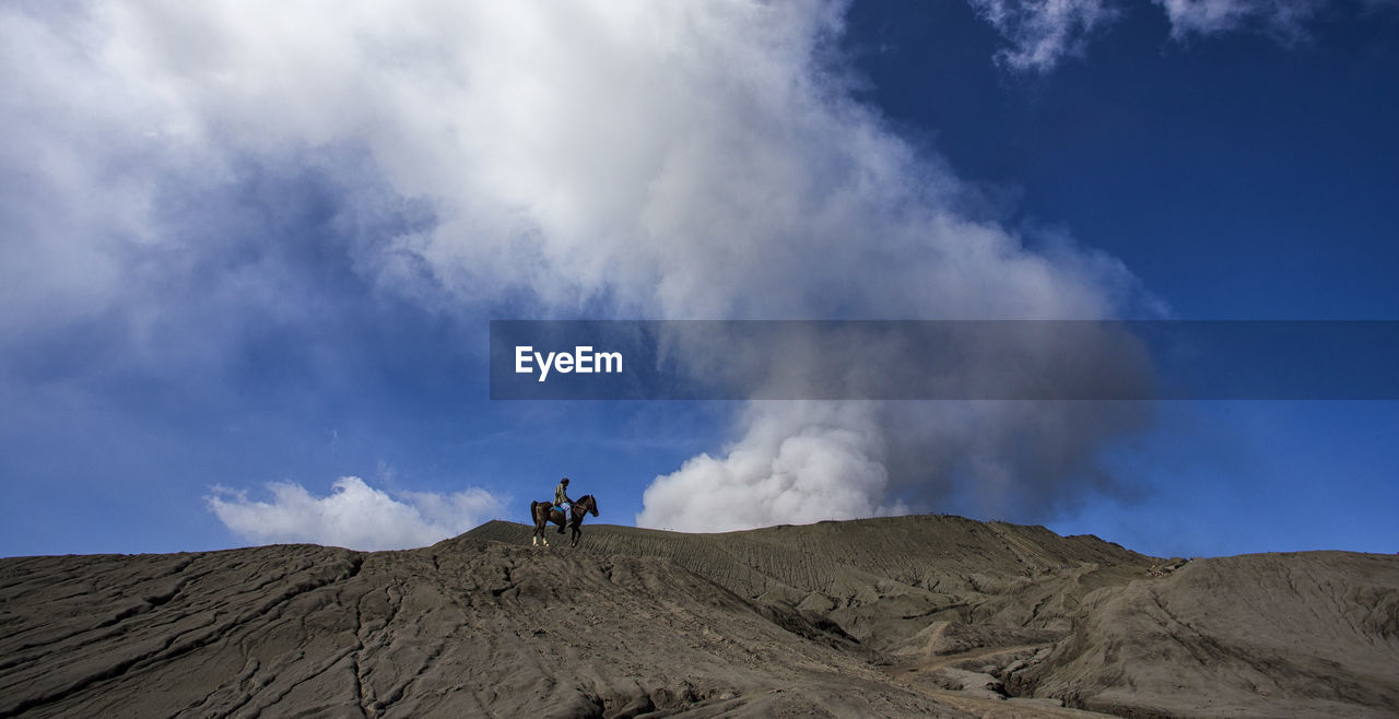 Mid distance view of person riding horse at mt bromo against blue sky